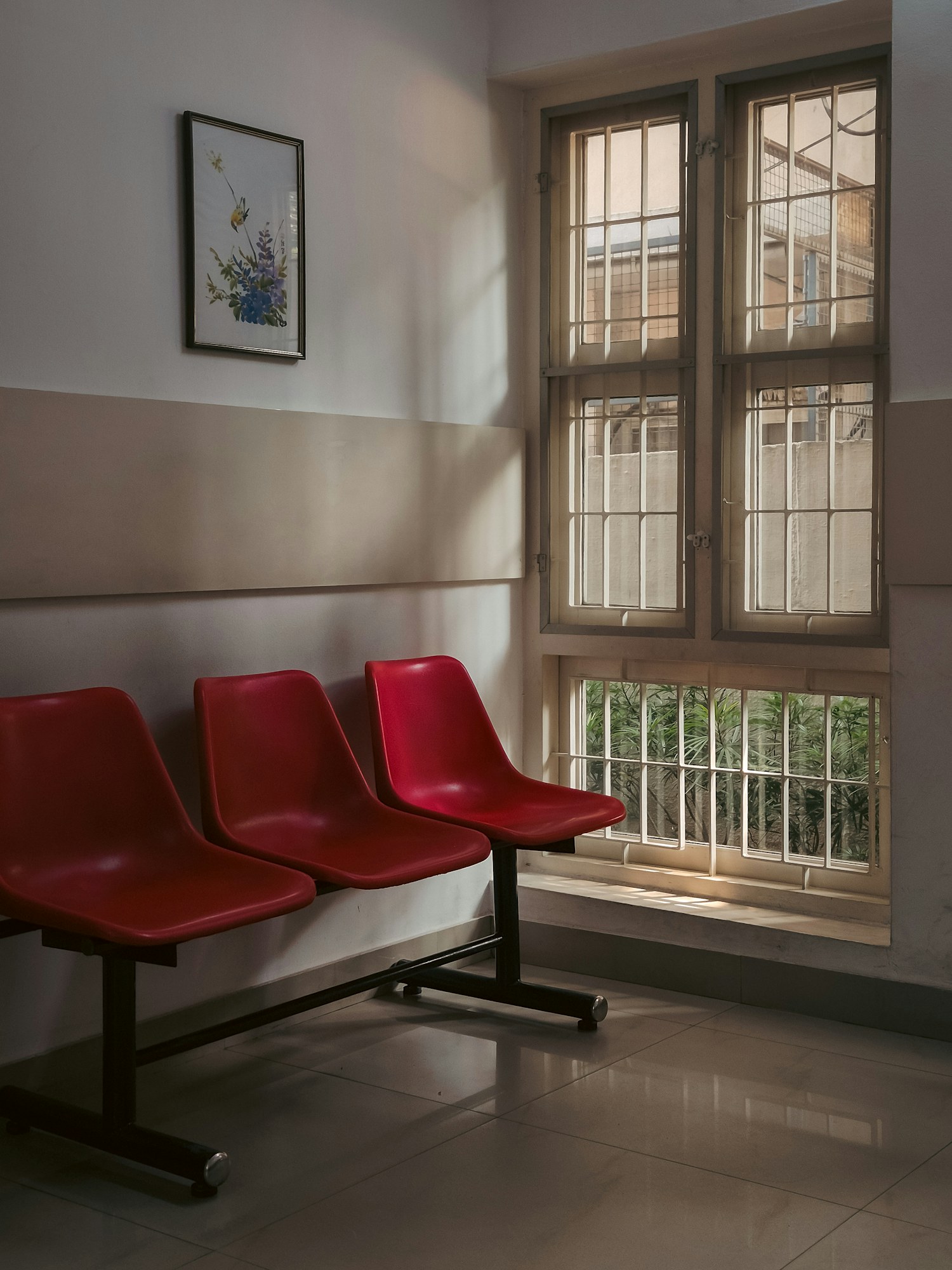 A quiet clinic waiting room with red chairs beside a large window.